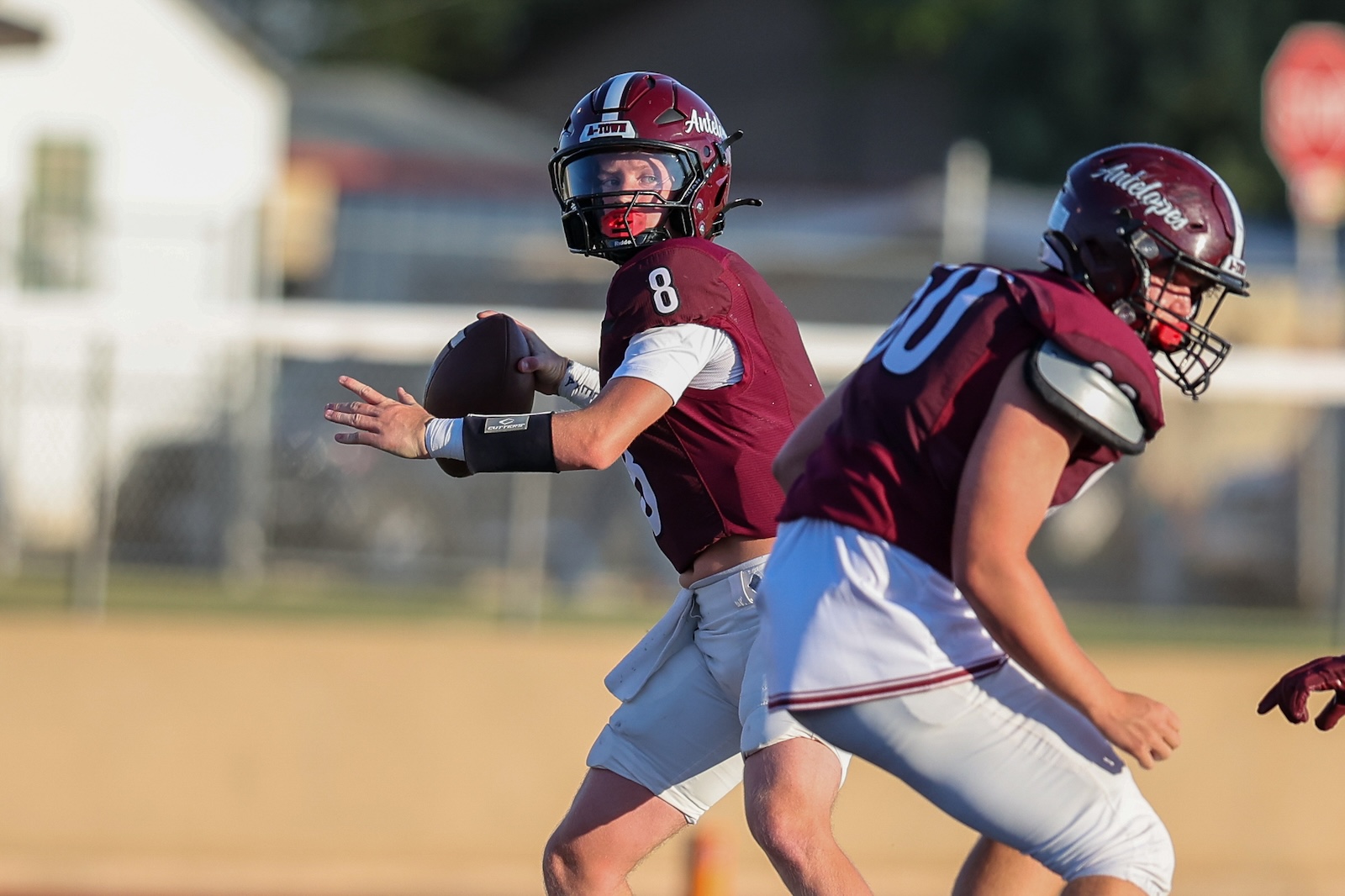 Quarterback in maroon jersey (#8) prepares to throw a football during a sunny game, other player in maroon jersey nearby.