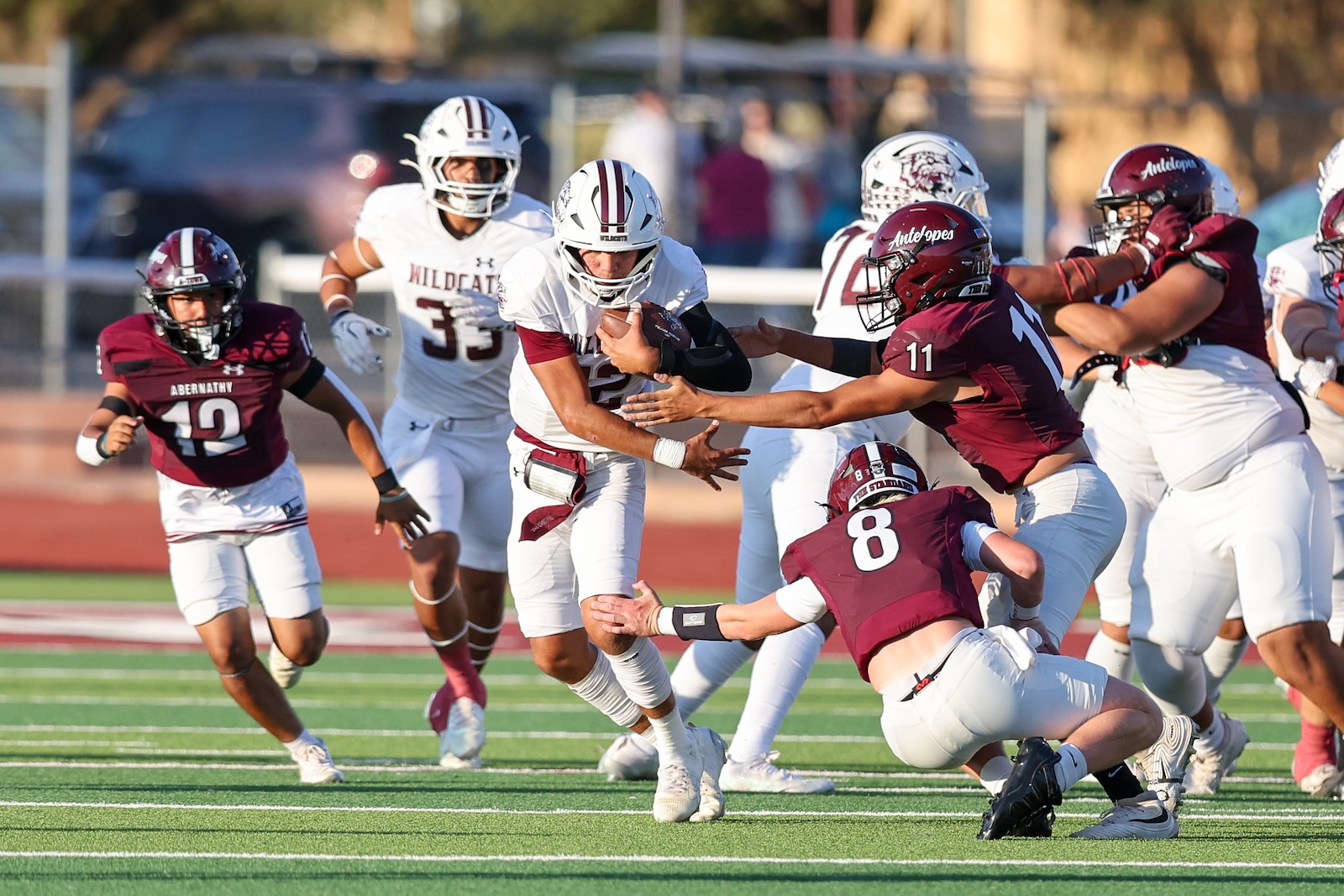 Abernathy Wildcats ball carrier in white breaks through maroon-clad defenders on a sunny football field.