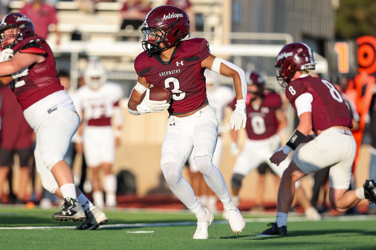 Football player in maroon Abernathy uniform (number 3) runs with ball toward the end zone while teammates block nearby on a sunny field.