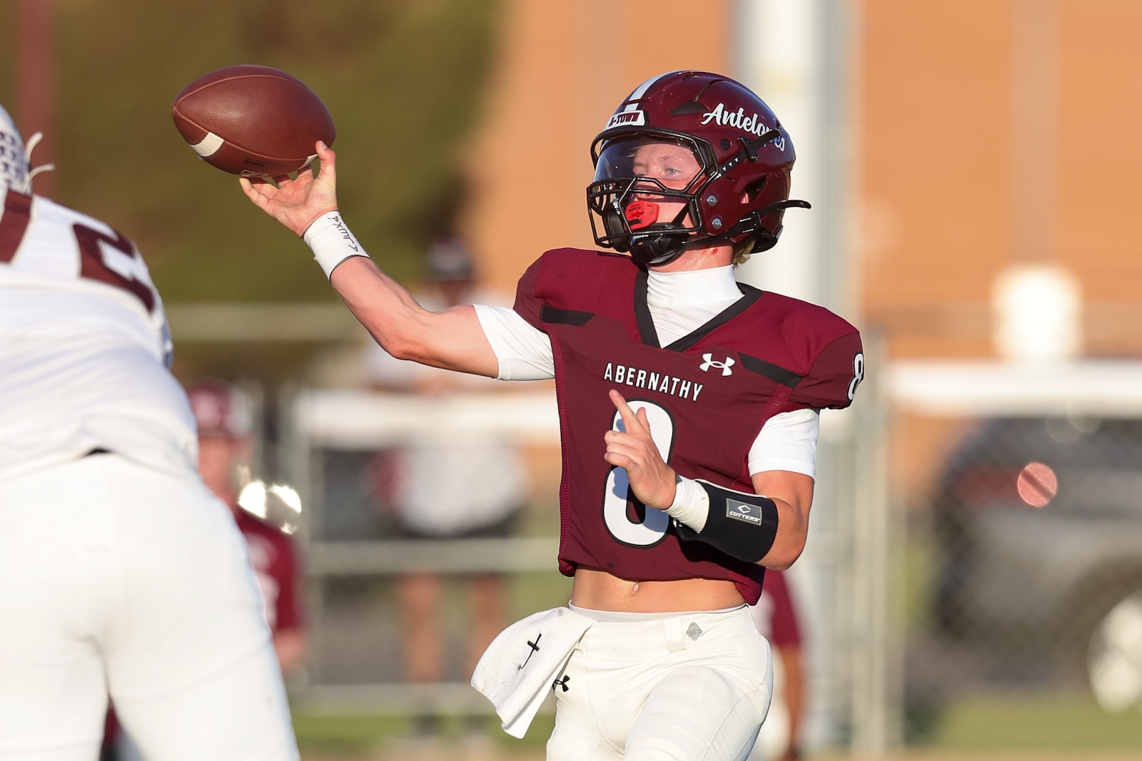 Quarterback in maroon Abernathy jersey throws a pass during a game on a sunny field.