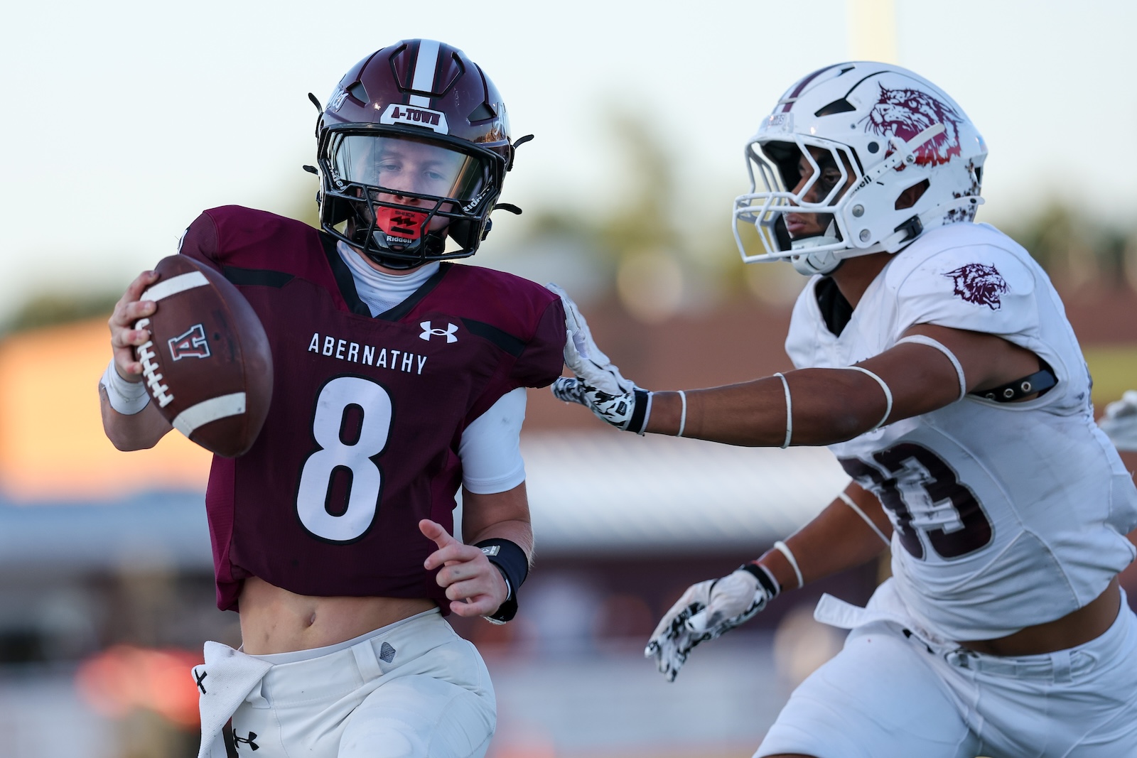 Quarterback in maroon Abernathy jersey #8 holds the ball while a defender in white reaches in for a tackle on a sunny field.