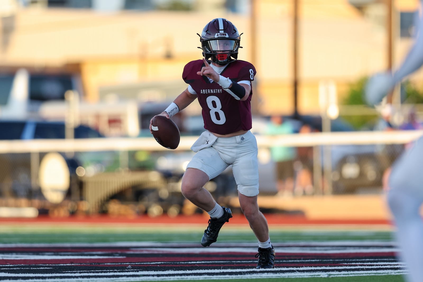 Quarterback in maroon jersey number 8 runs with the football, looking for a throwing lane on a football field.