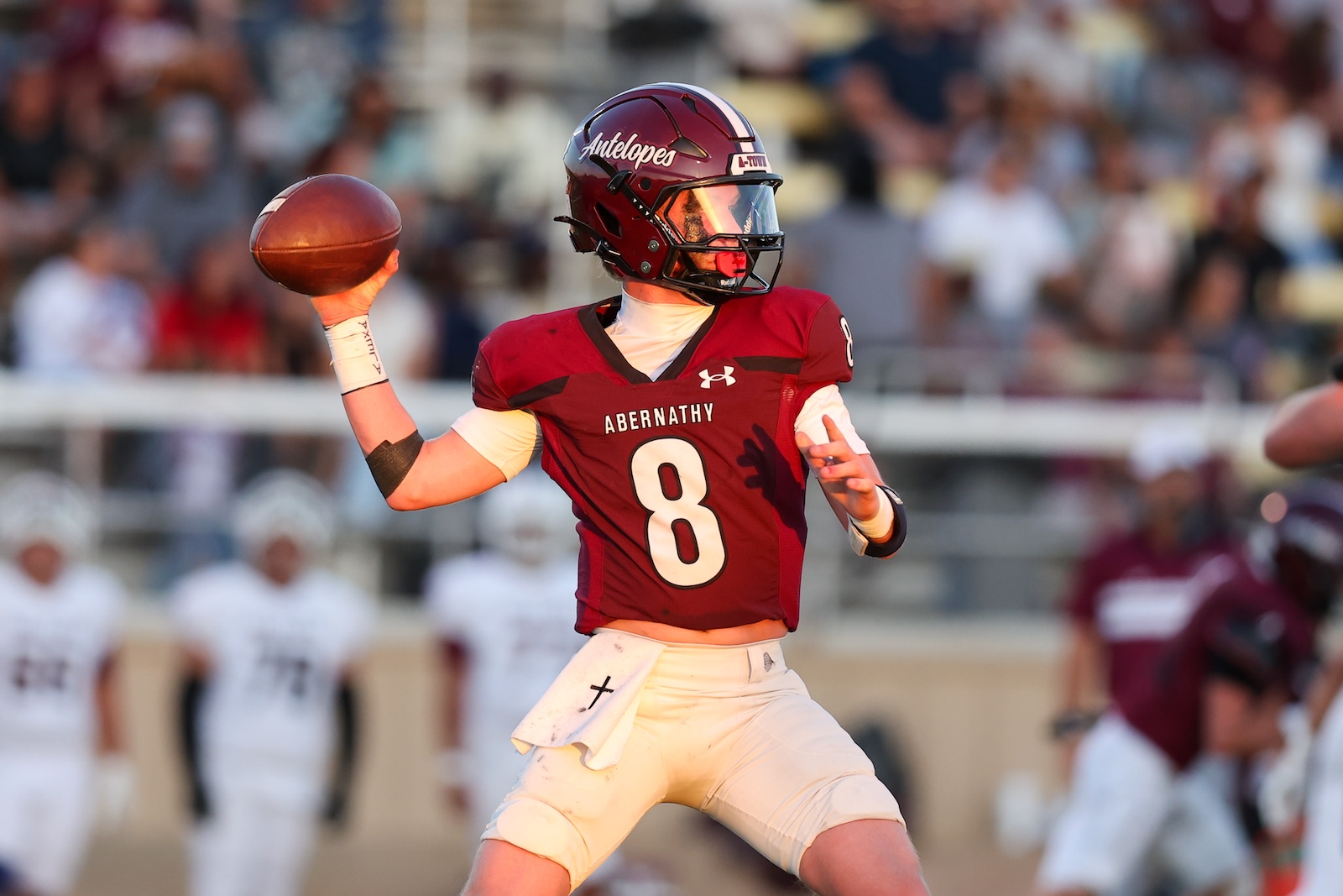 Quarterback in maroon Abernathy jersey (number 8) mid-throw during a football game with blurred stands in the background.