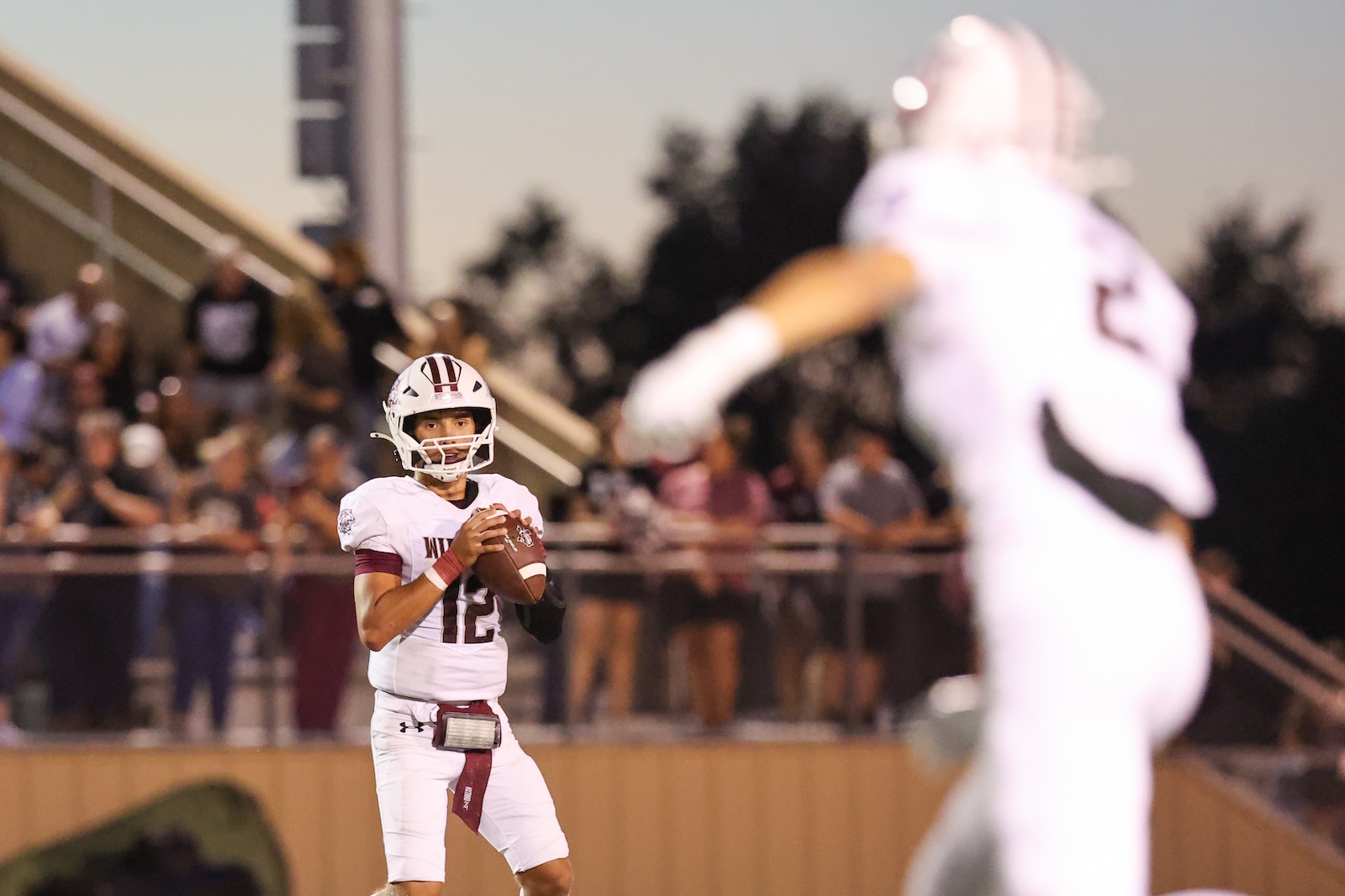 Quarterback in white uniform #12 holds a football, ready to throw during a game.