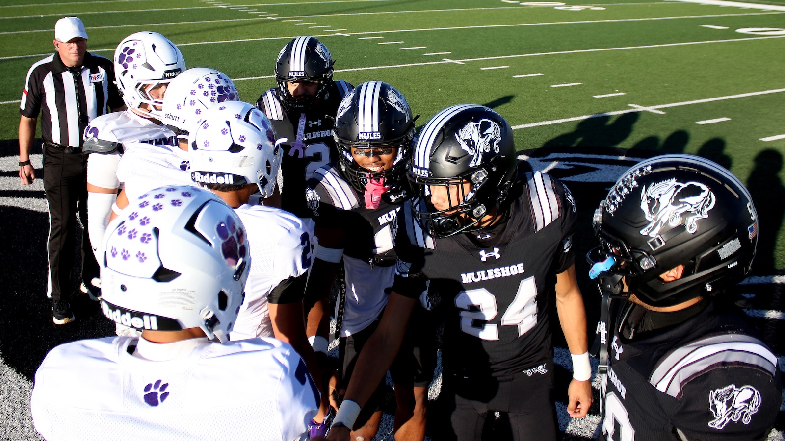 Muleshoe football players in black and white uniforms huddle on the field before kickoff.