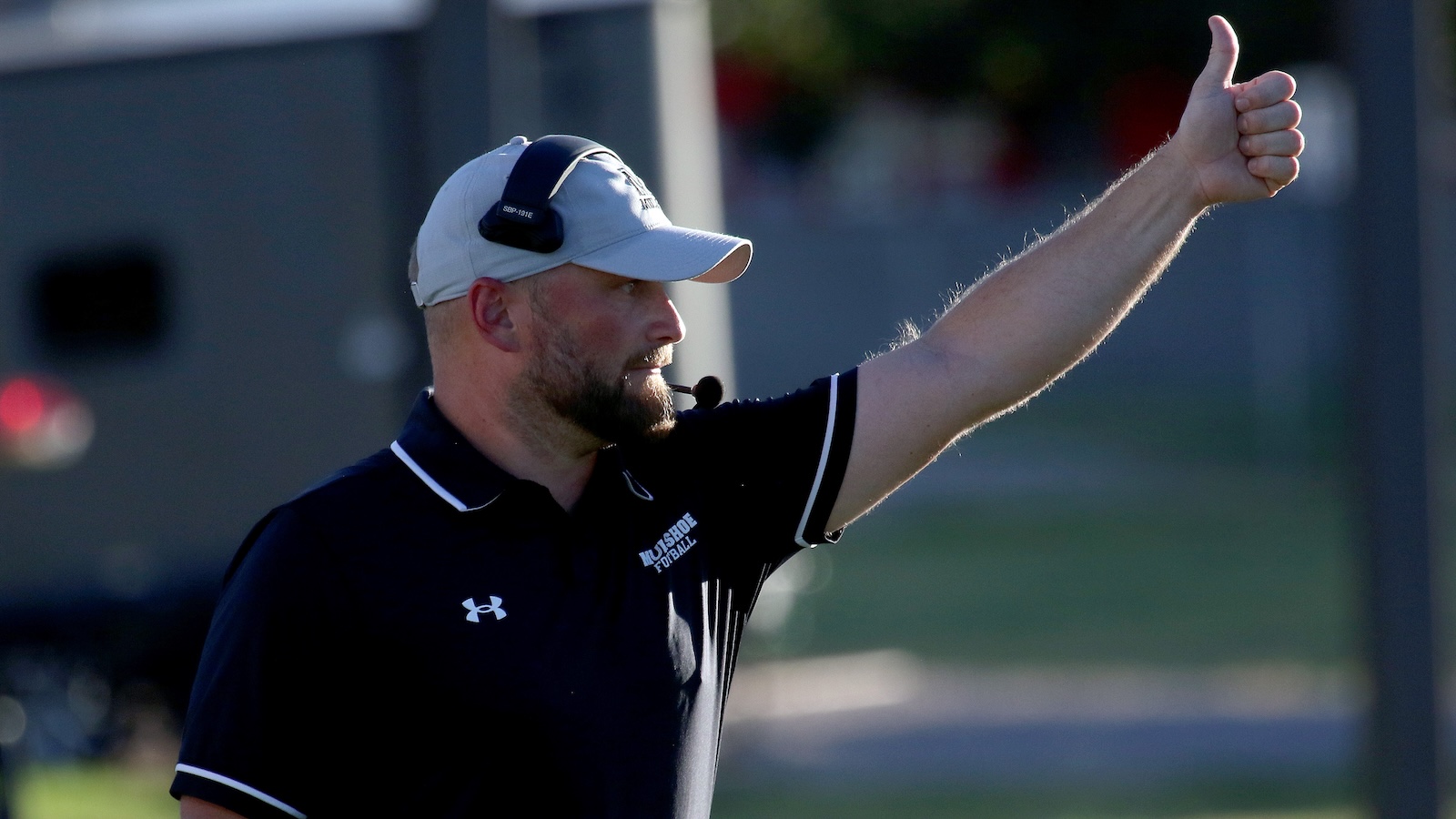 Coach in a white cap and headset giving a thumbs-up on the sideline
