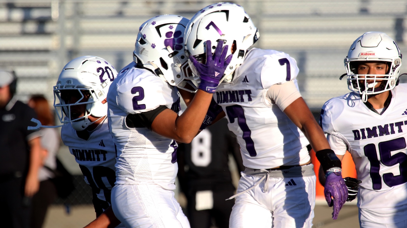 White-and-purple Dimmit football players celebrate a play on the field, hugging and high-fiving.