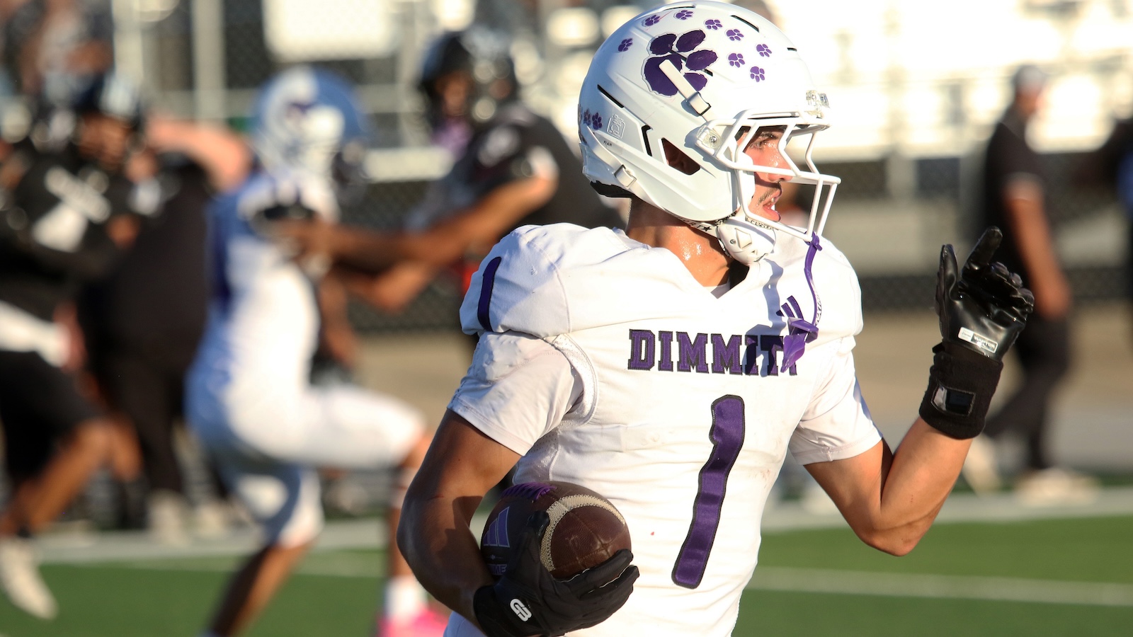 Football player in white and purple (number 1) runs with the ball during a game, wearing a paw-print helmet and gloves.