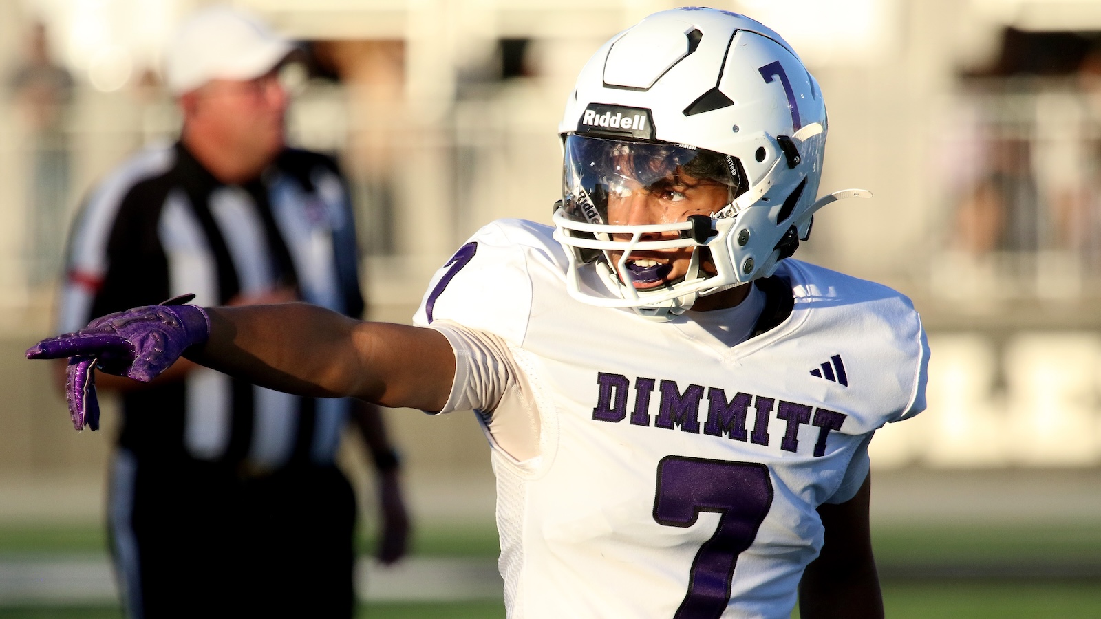 Football player in white helmet and purple gloves points during a play; jersey says DIMMITT #7.