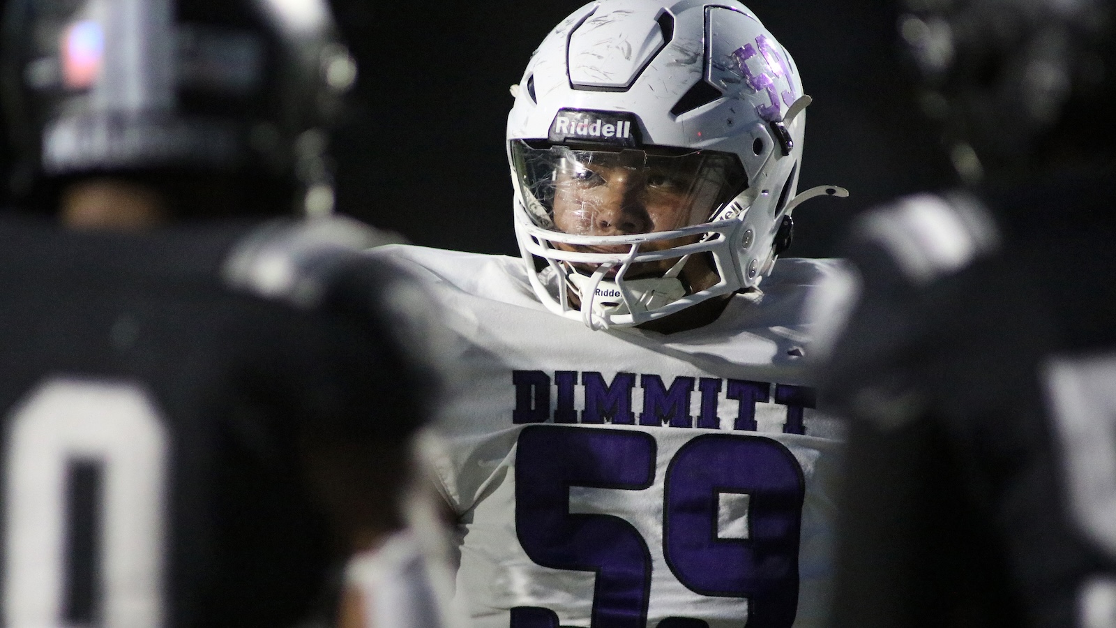 American football player in a white jersey with purple number 59 and DIMMIT across the chest, helmet on, looking forward.
