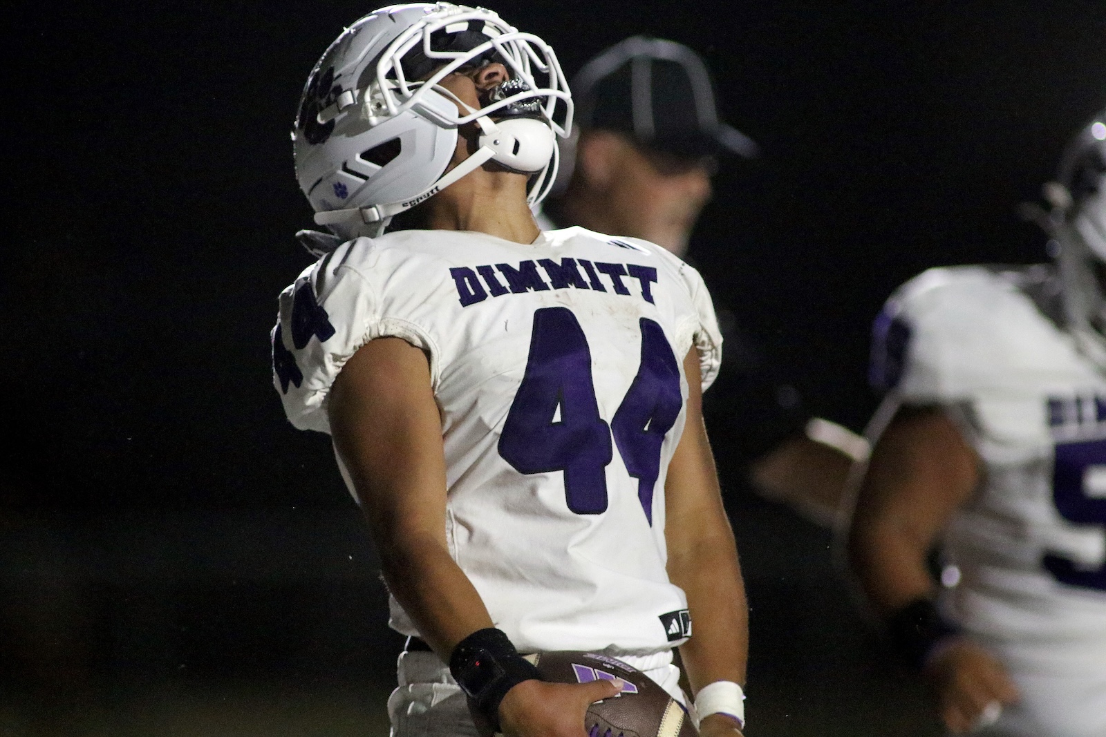Football player in a white jersey with'DIMMIT' and number 44, holding a football at night.