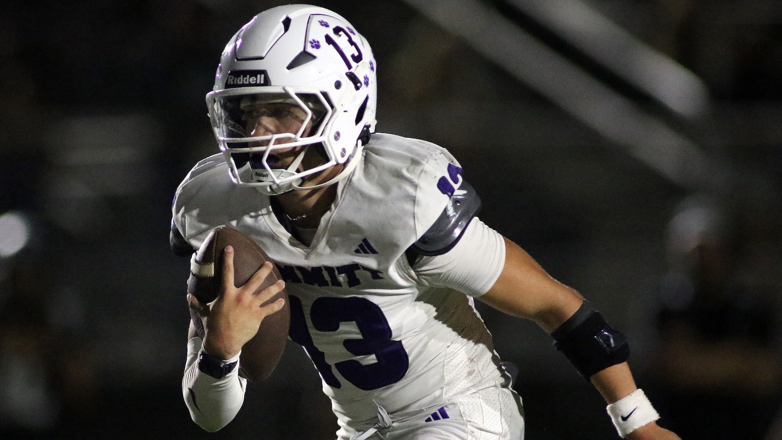 Football player in a white uniform with purple number 13 running with the ball during a game.