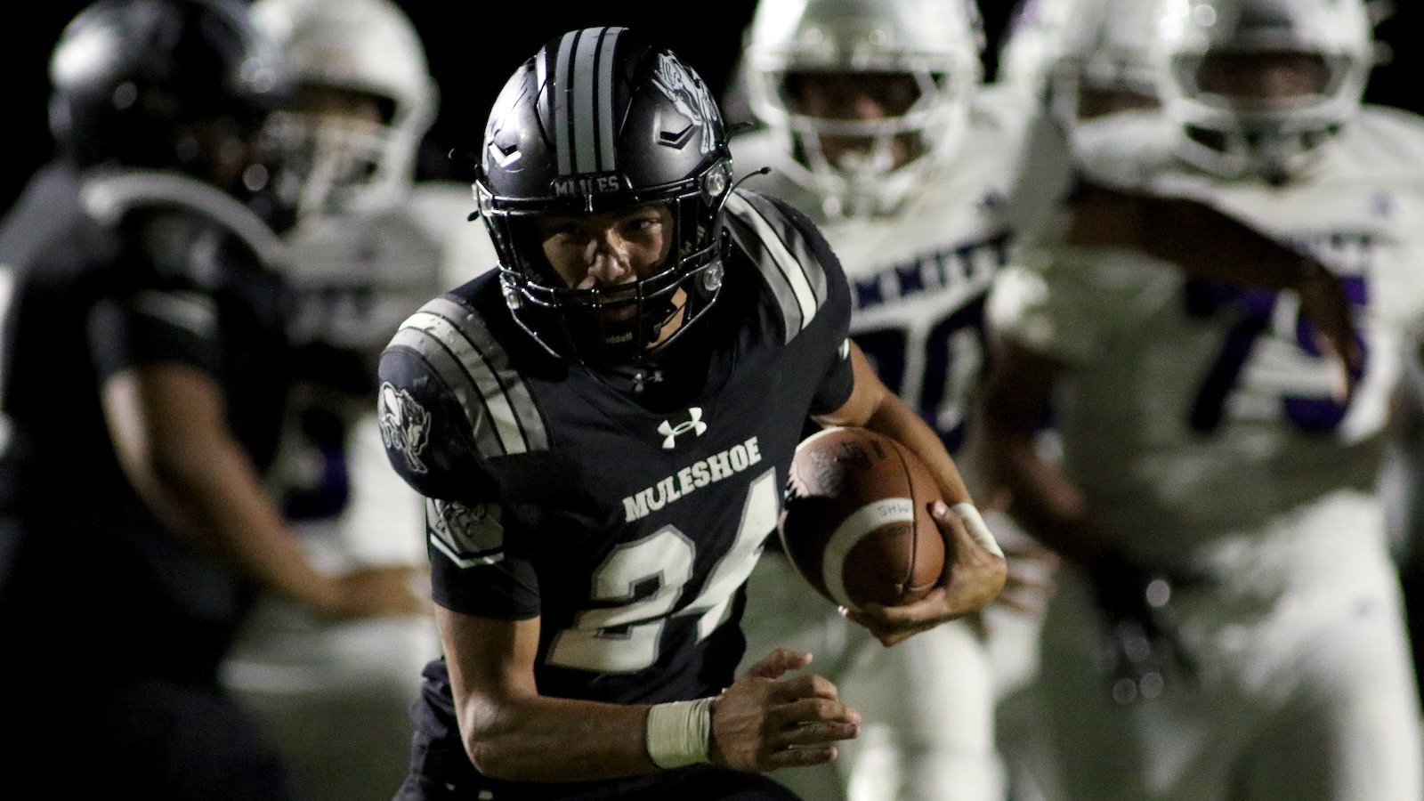 Muleshoe football player in dark uniform #21 sprints with the ball as defenders chase in the background.