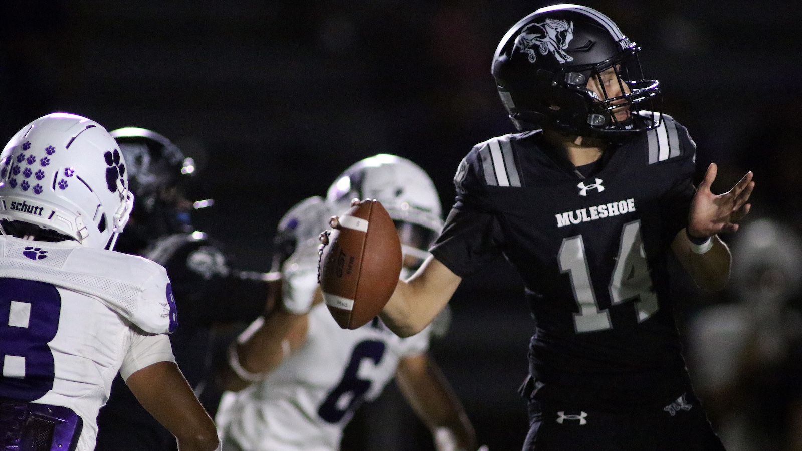 MULESHOE quarterback, #14, throws a pass at night with teammates nearby in white jerseys.