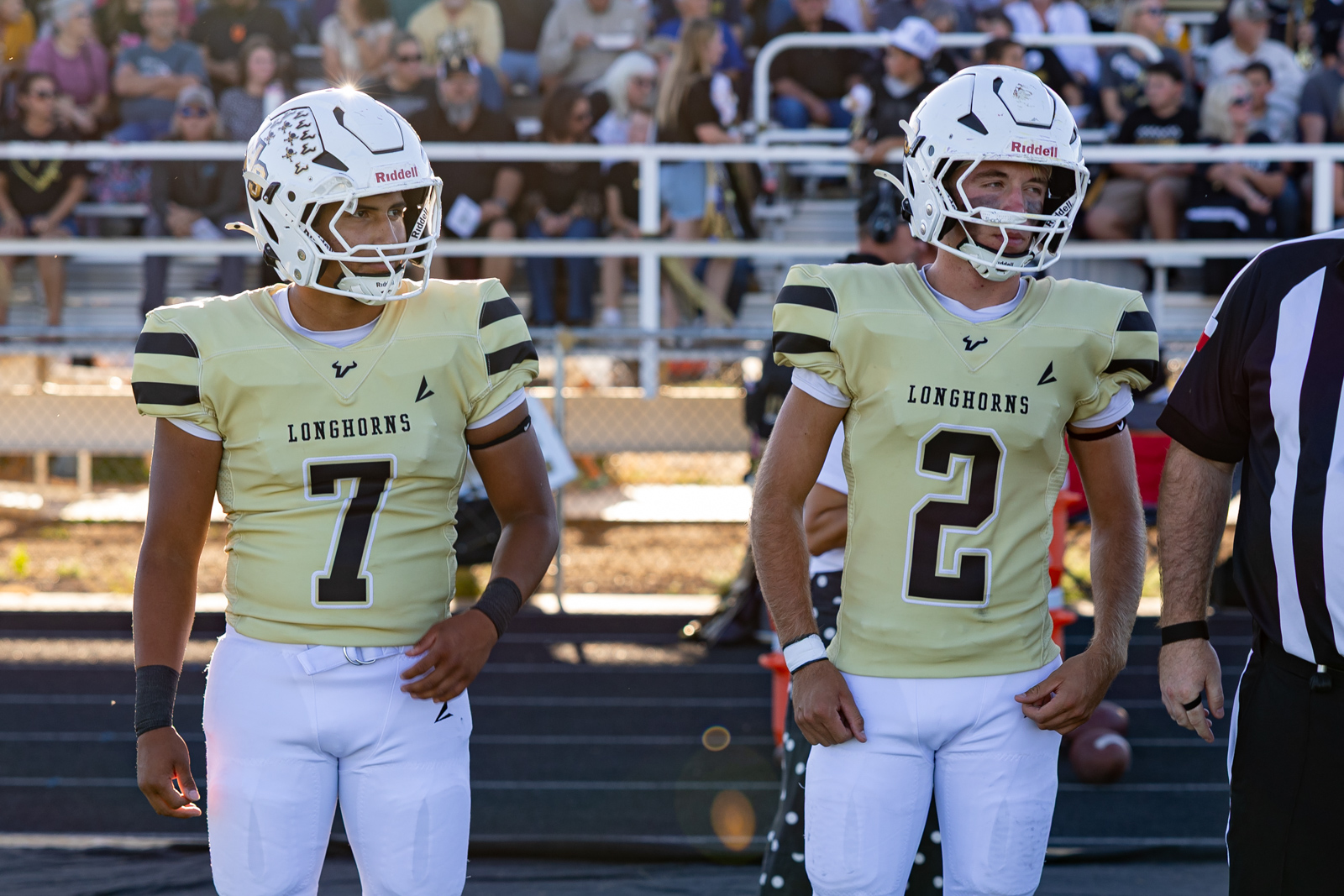 Two football players in cream Longhorns jerseys, numbers 7 and 2, stand on the sideline with white helmets and pads.