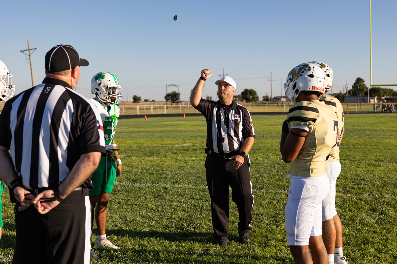 Referee tossing a coin before a football game as players stand ready on the field under a clear blue sky