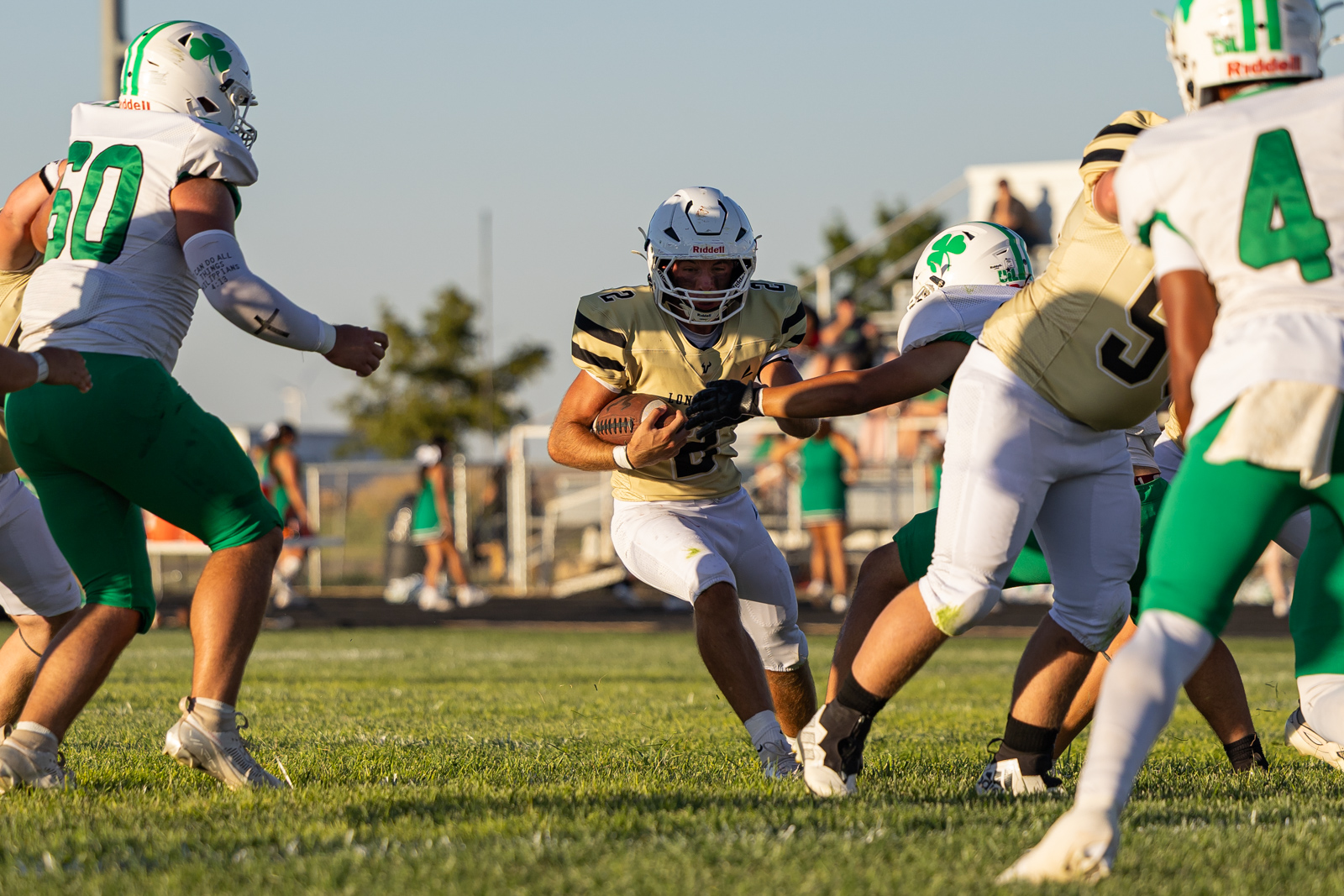 A football player in gold jersey runs with the ball as defenders close in on a grassy field.