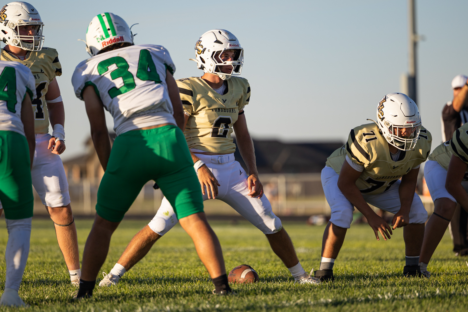 Youth football game at the line of scrimmage with players in gold and white uniforms ready to snap the ball at center field edge of the grass.