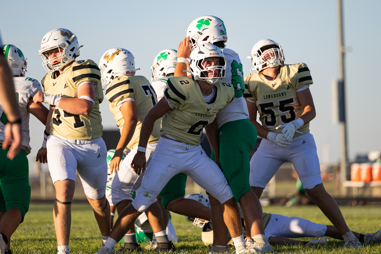 Group of football players in gold uniforms and white helmets collide on a grassy field during a game, mid-action.
