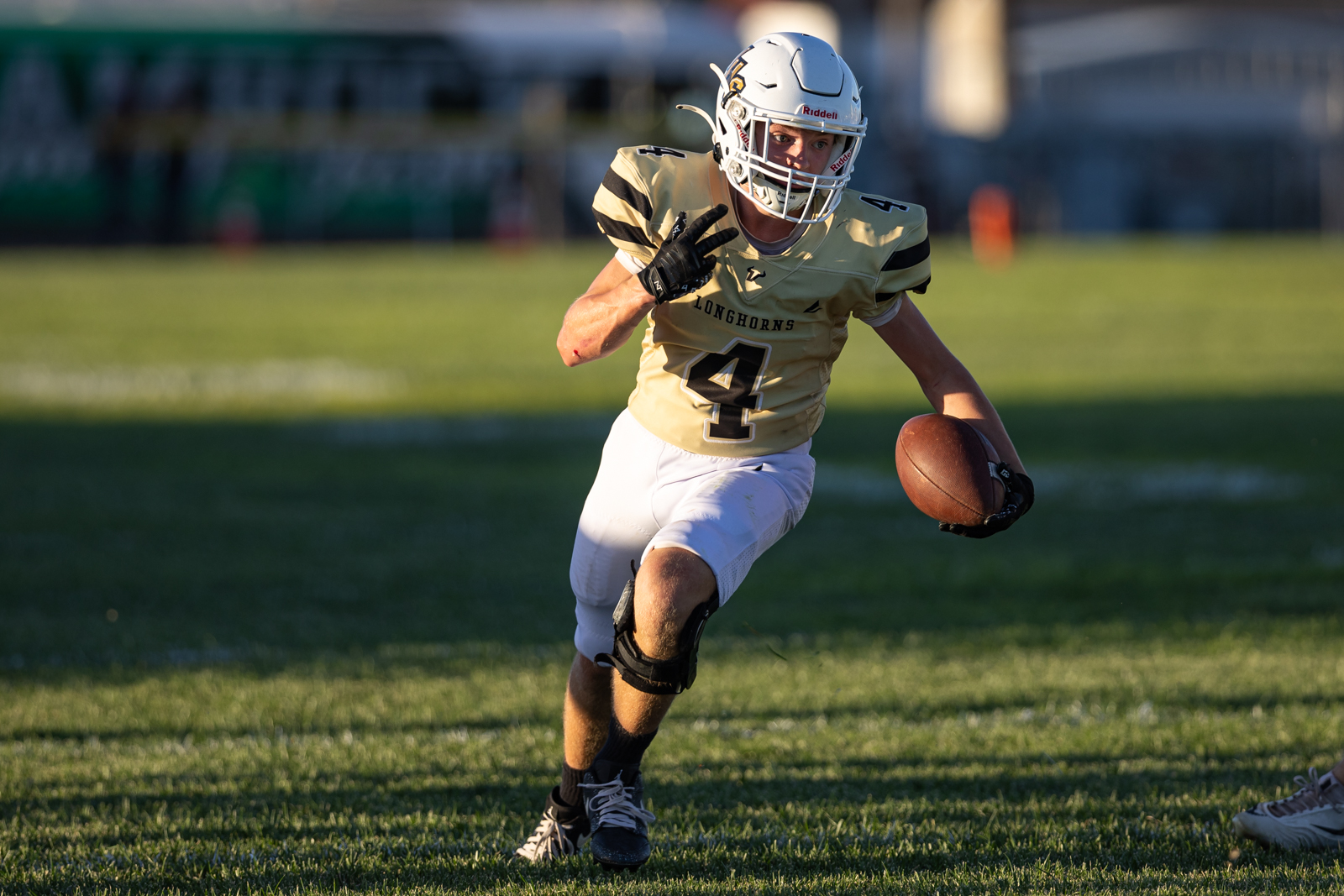 American football player wearing a gold jersey with number 4, running with the ball on a grass field