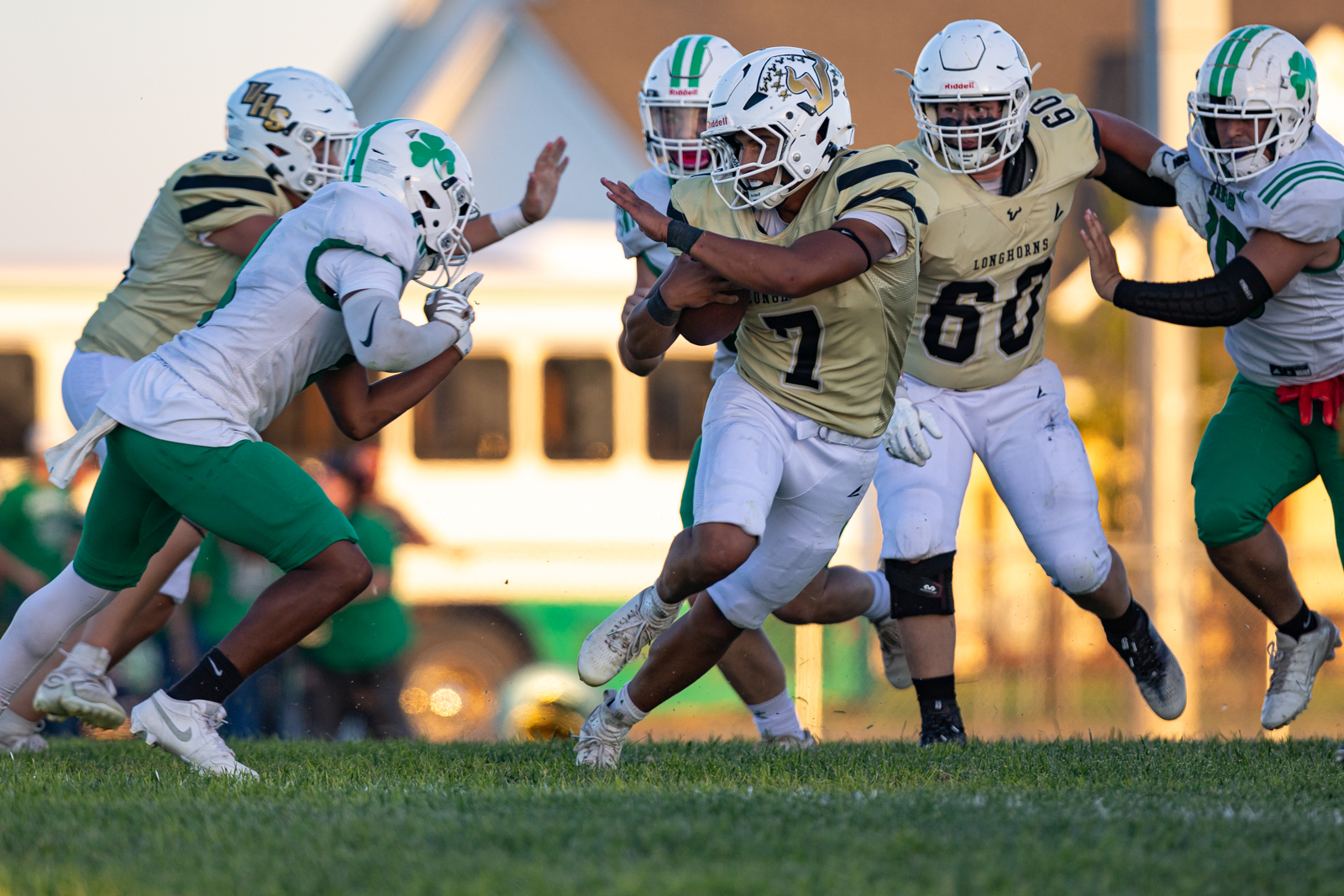 Running back in gold and white carries the football as defenders in white and green close in on a grassy field.