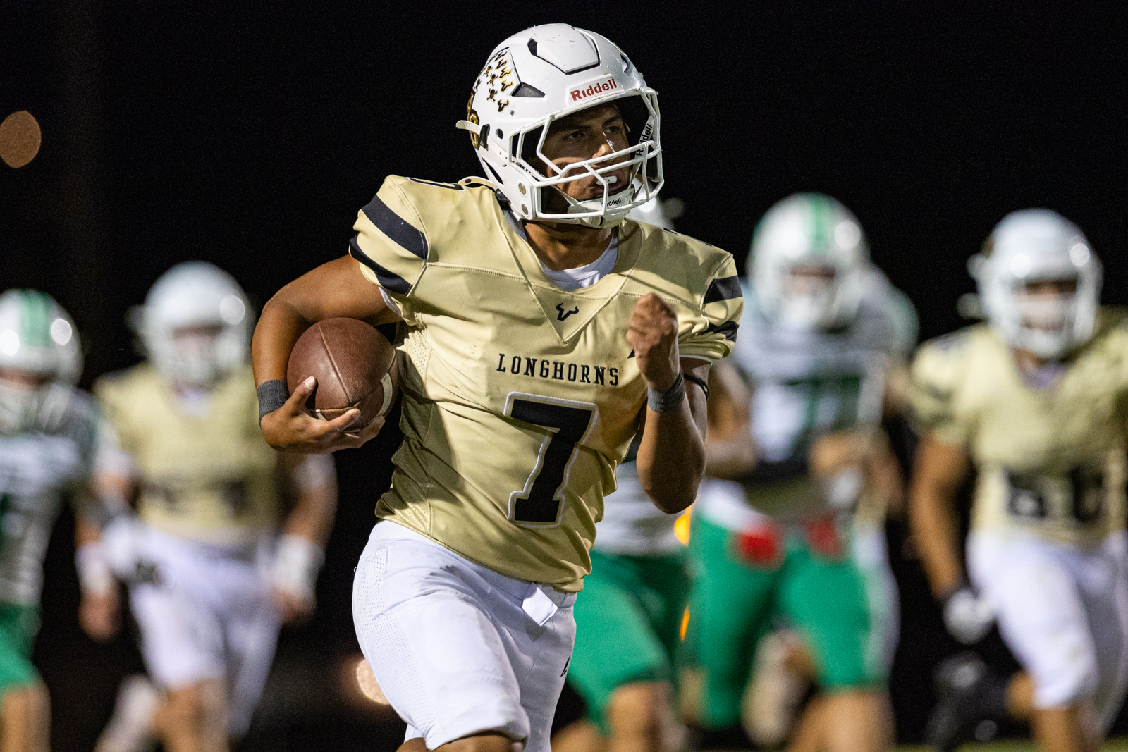 Football player in a gold Longhorns jersey (number 7) runs with the ball during a night game, defenders in the background.