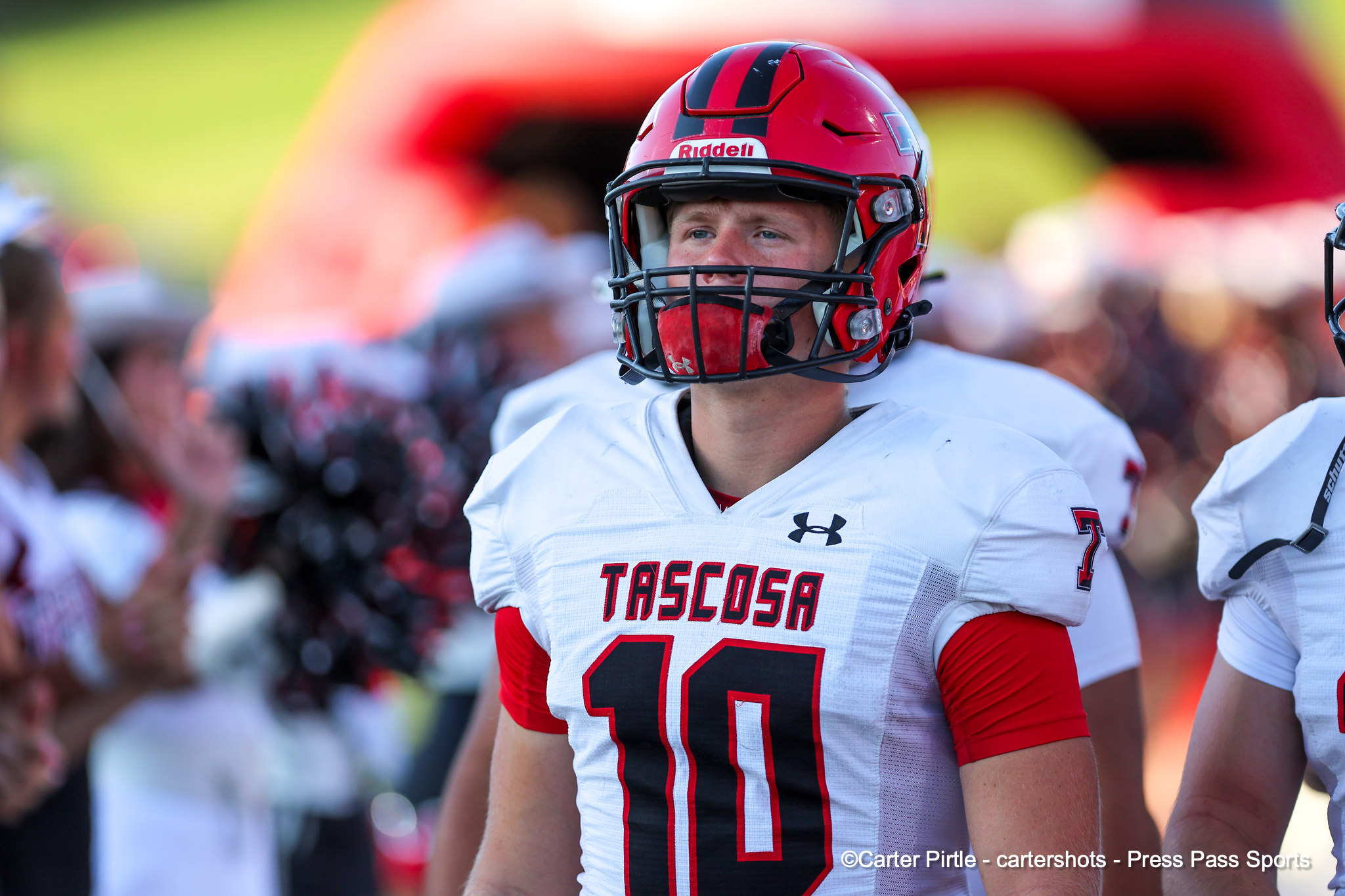 Tascosa football player wearing a red helmet and white jersey with number 10 on the sidelines, crowd in the background.