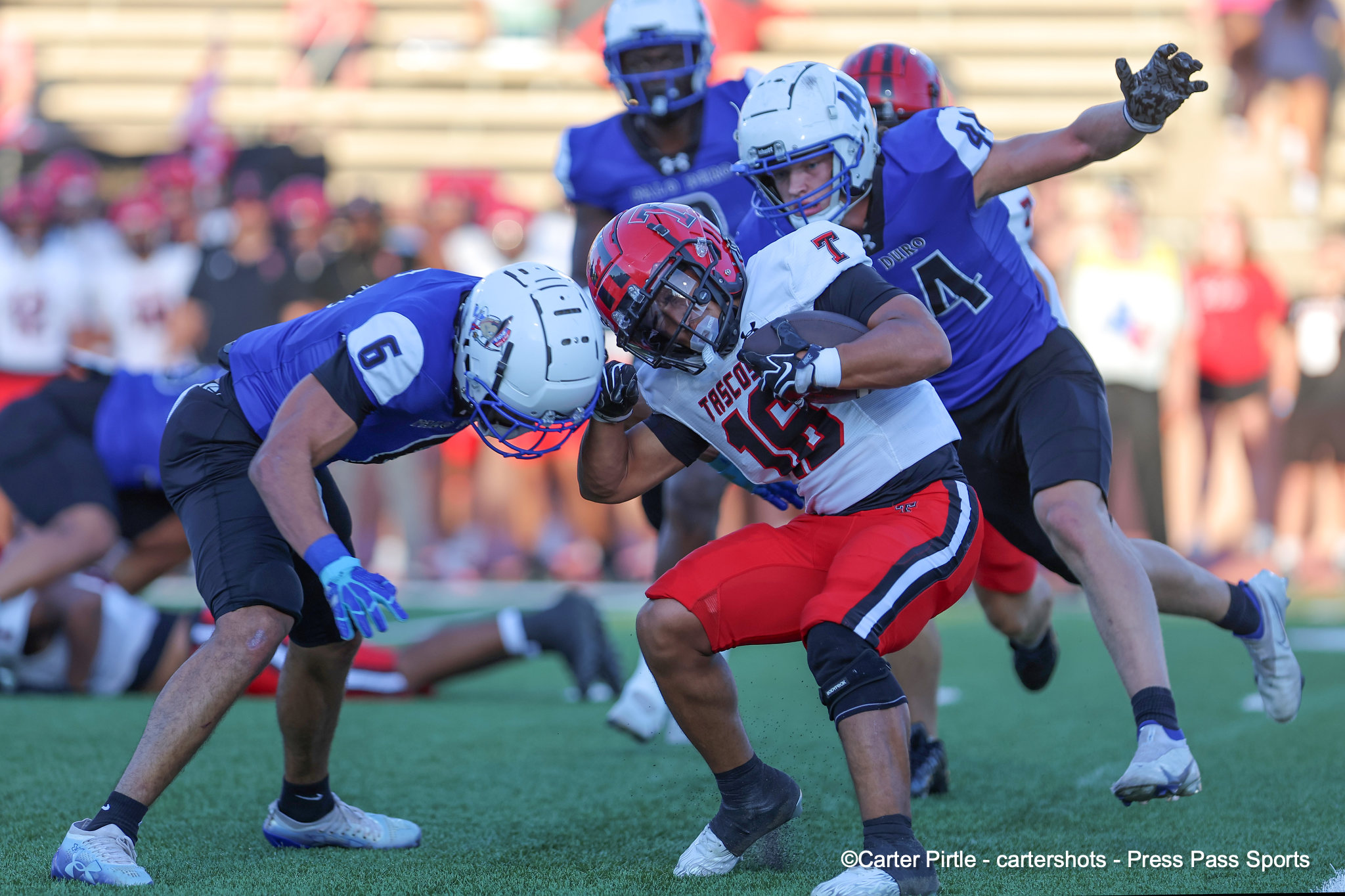 Football players in purple jerseys tackle a ball carrier in white and red on a grassy field during a game.