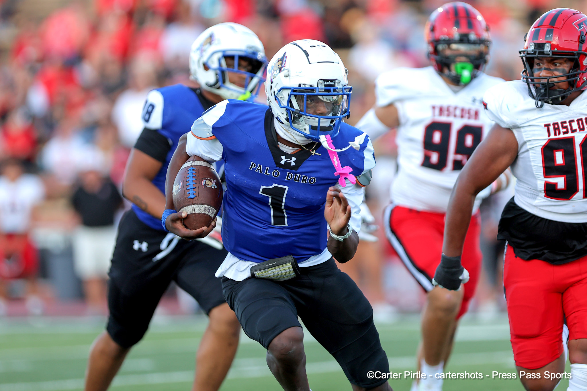 Palo Duro player in blue with the ball runs forward as white-jersey defenders close in.