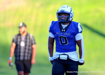 20260911-Tascosa-PaloDuro-FB-015 | Press Pass Sports Football player in blue Palo Duro jersey and helmet on the field, smiling, with blurred teammate in background.