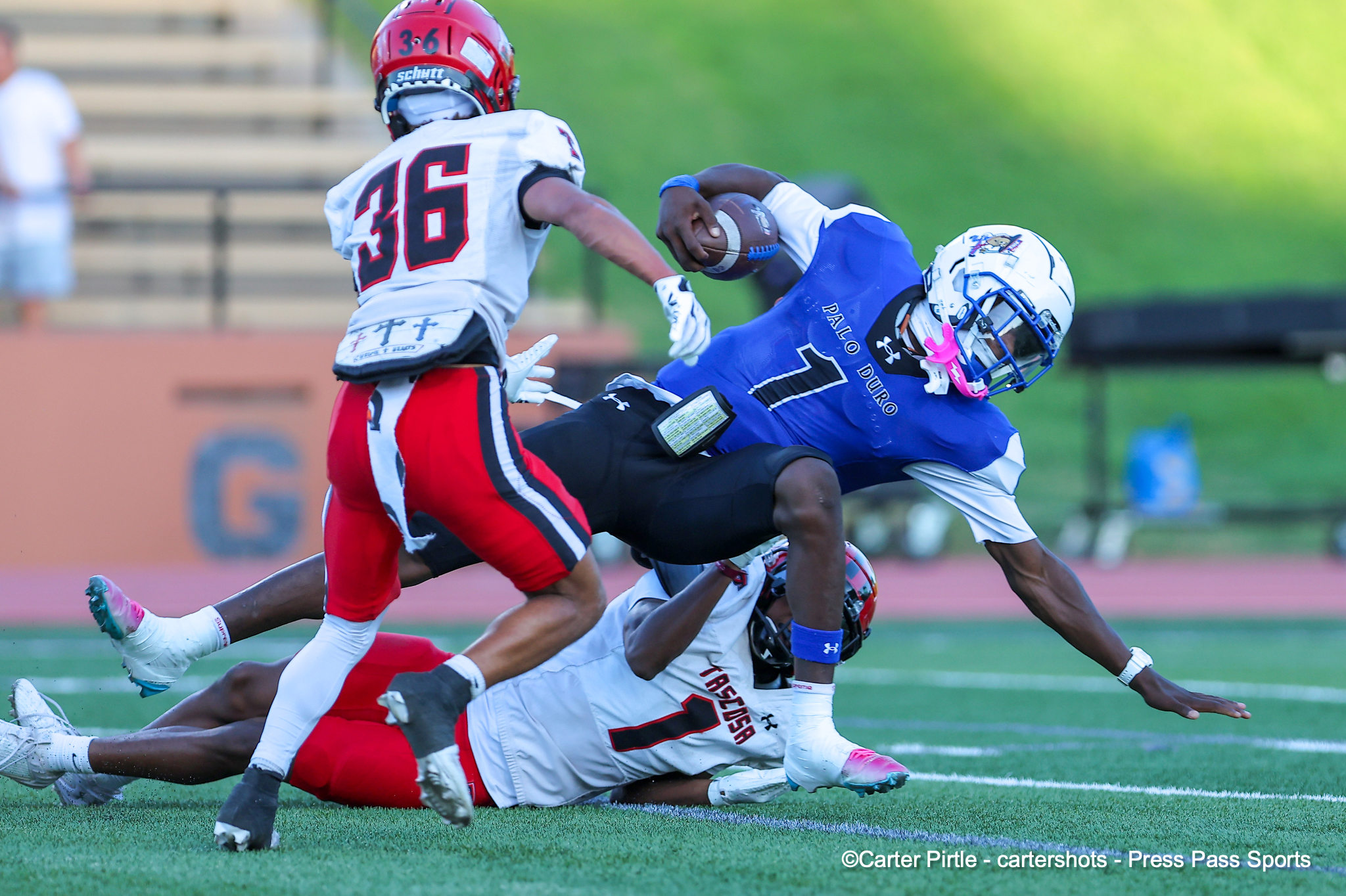 Blue-uniform player tackling a white-uniform opponent with red numbers during a football play on a grassy field.