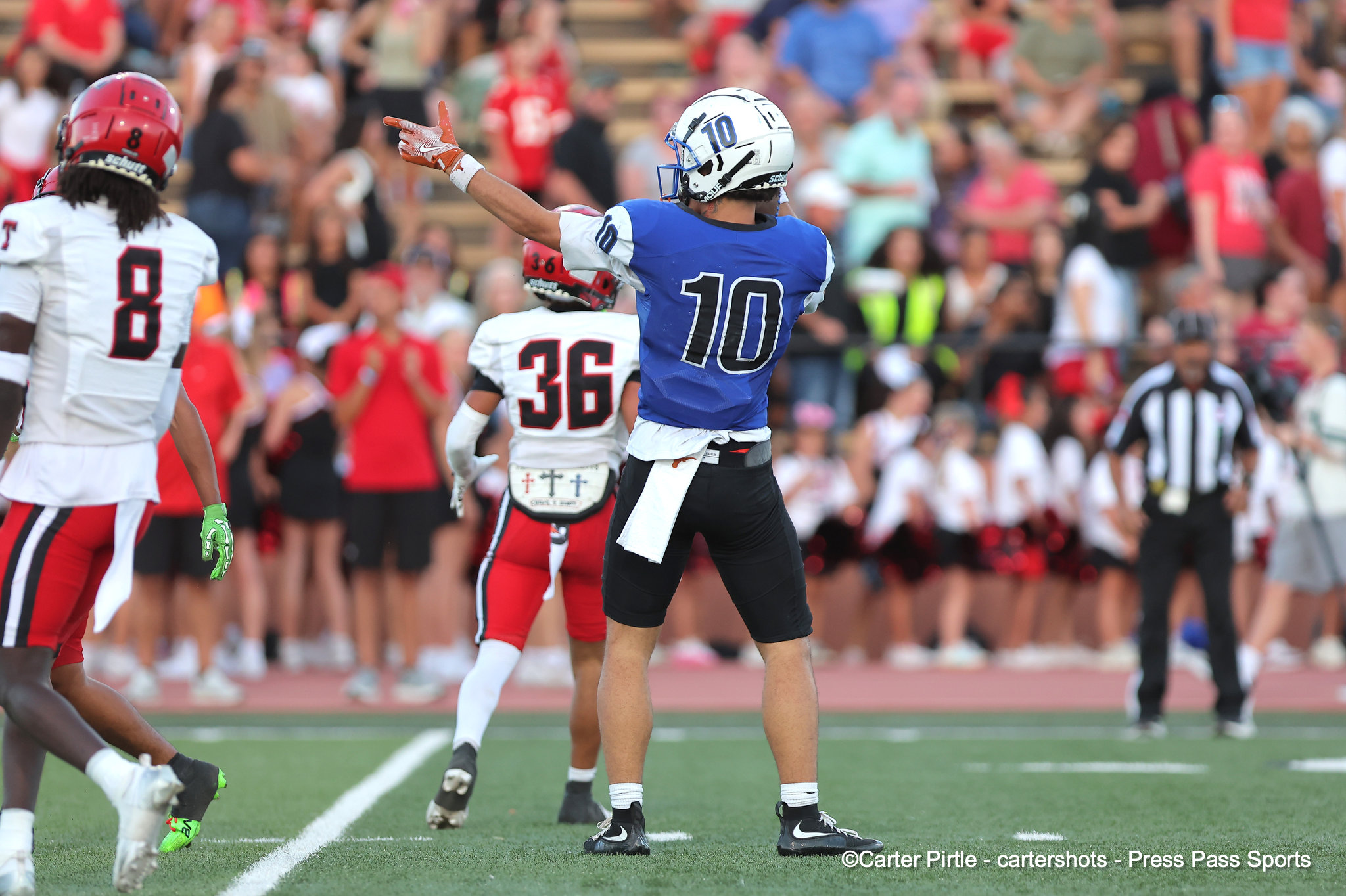 Football player in blue jersey #10 raises arms in celebration on a football field, with teammates and a cheering crowd in the background