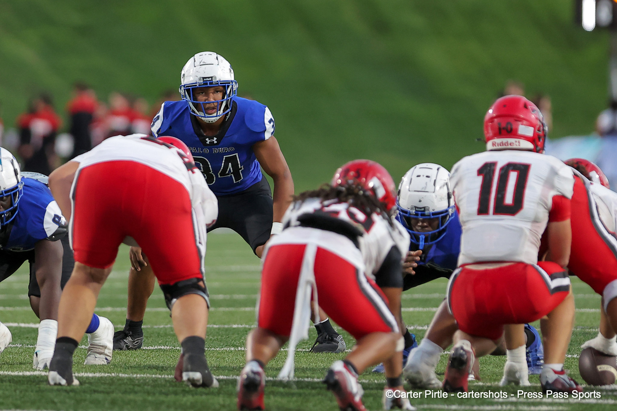 American football players at the line of scrimmage; blue team with number 84 near the center, facing red and white defenders on a green field.