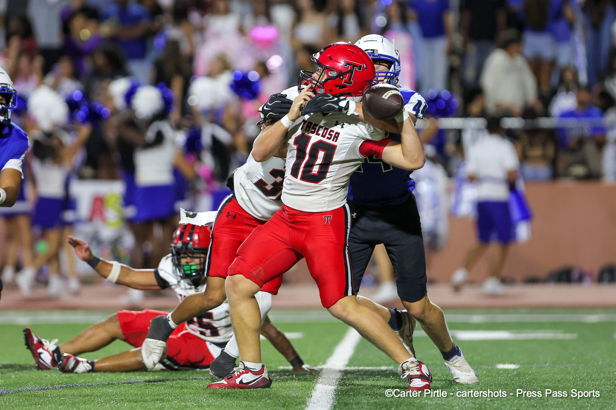 Two football players collide while chasing the ball on a crowded field, wearing red and white uniforms.