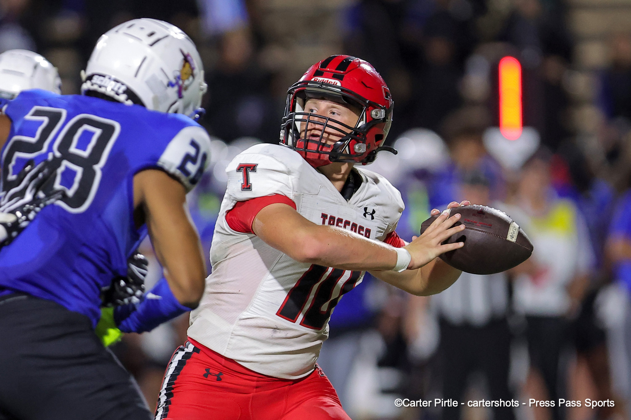 Football player in white and red uniform holds the ball and looks for a lane as a defender in blue approaches.