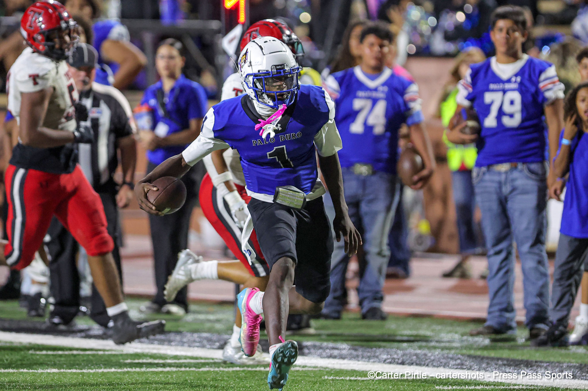 Football player in a blue Palo Duro jersey (#1) runs with the ball during a high school game, with spectators in the background.