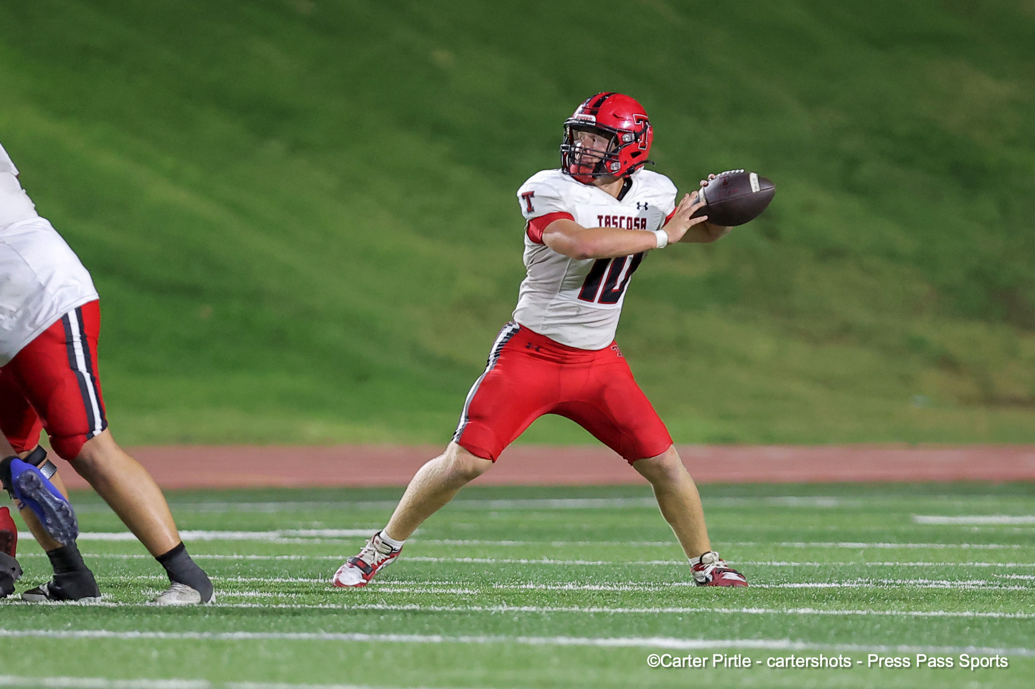 Football player in white and red catching a football on a green field during a game at dusk/dusk-like lighting.