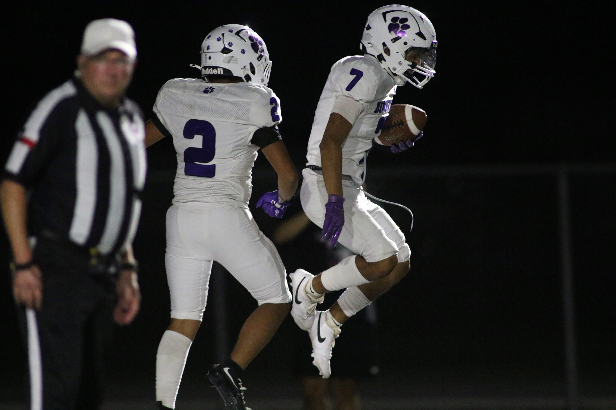 Dimmitt vs Muleshoe - Diego Cortez Punt Return TD | Press Pass Sports Two football players in white uniforms with purple numbers leap in the air at night, one carrying the ball as the other approaches nearby.