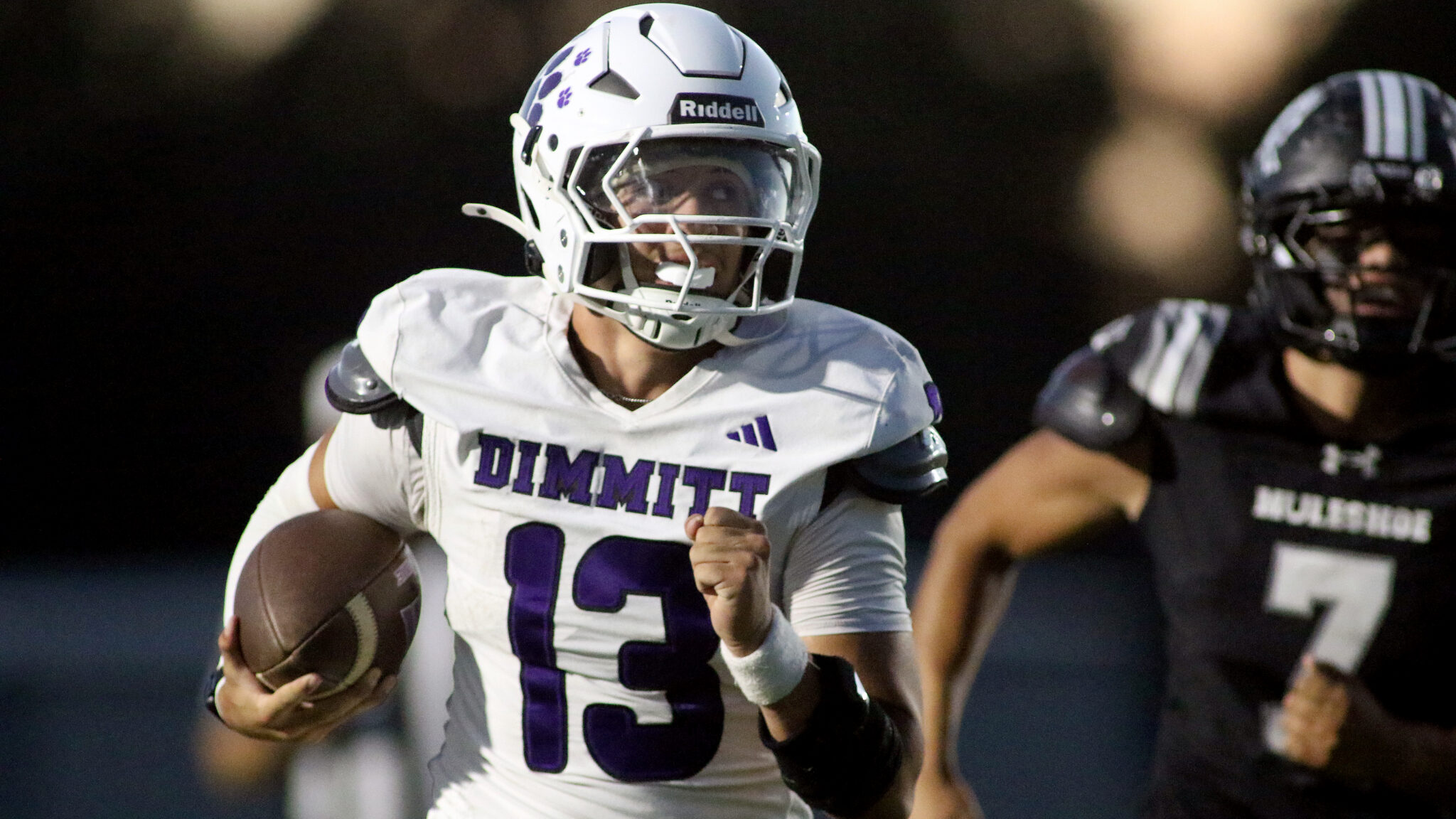 Dimmitt vs Muleshoe - Kaden Carpio | Press Pass Sports Football player in white Dimmit jersey (#23) runs with the ball, helmet on, during a game with a black-uniform opponent in the background
