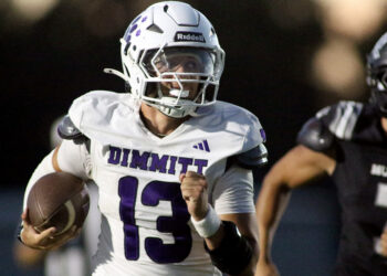 Football player in white Dimmit jersey (#23) runs with the ball, helmet on, during a game with a black-uniform opponent in the background