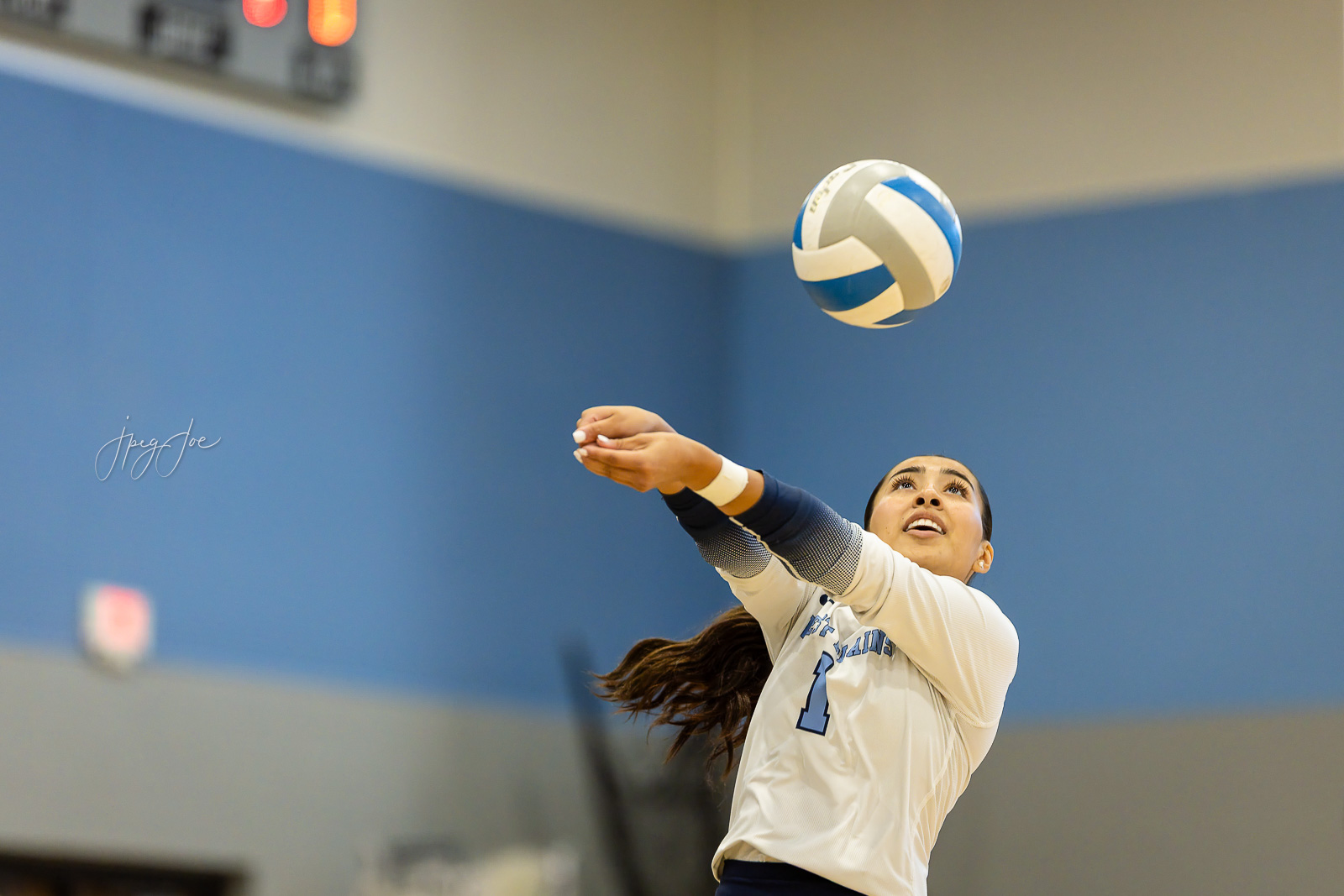 canyon-vs-west-plains-jpegJoe-volleyball-pps-3 | Press Pass Sports Female volleyball player in a white jersey reaches up to contact a blue-and-white ball in a gym.