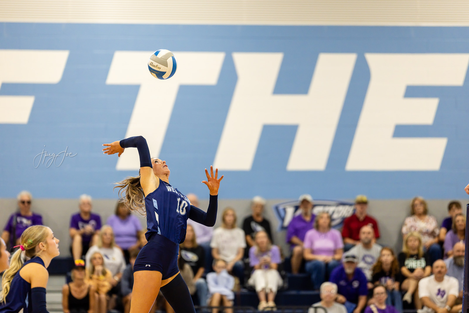 canyon-vs-west-plains-jpegJoe-volleyball-pps-4 | Press Pass Sports Female volleyball player in a navy uniform jumps to strike the ball in a gym with spectators watching from the bleachers.