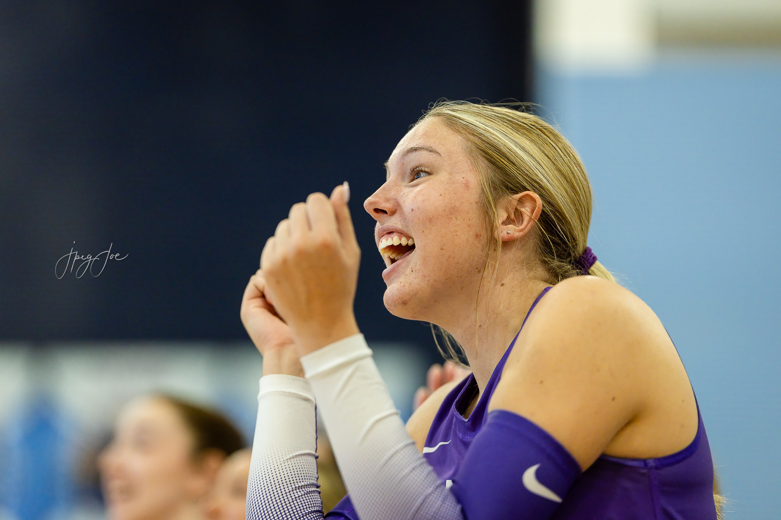 canyon-vs-west-plains-jpegJoe-volleyball-pps-11 | Press Pass Sports Young female athlete in a purple top cheerrs with hands together, smiling in a gym setting.
