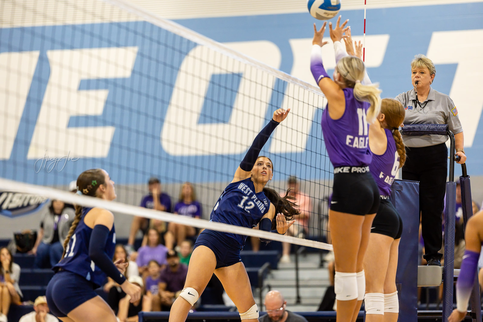 canyon-vs-west-plains-jpegJoe-volleyball-pps-13 | Press Pass Sports Volleyball action: a blue-team hitter (#12) spikes the ball at the net as purple blockers attempt to block.