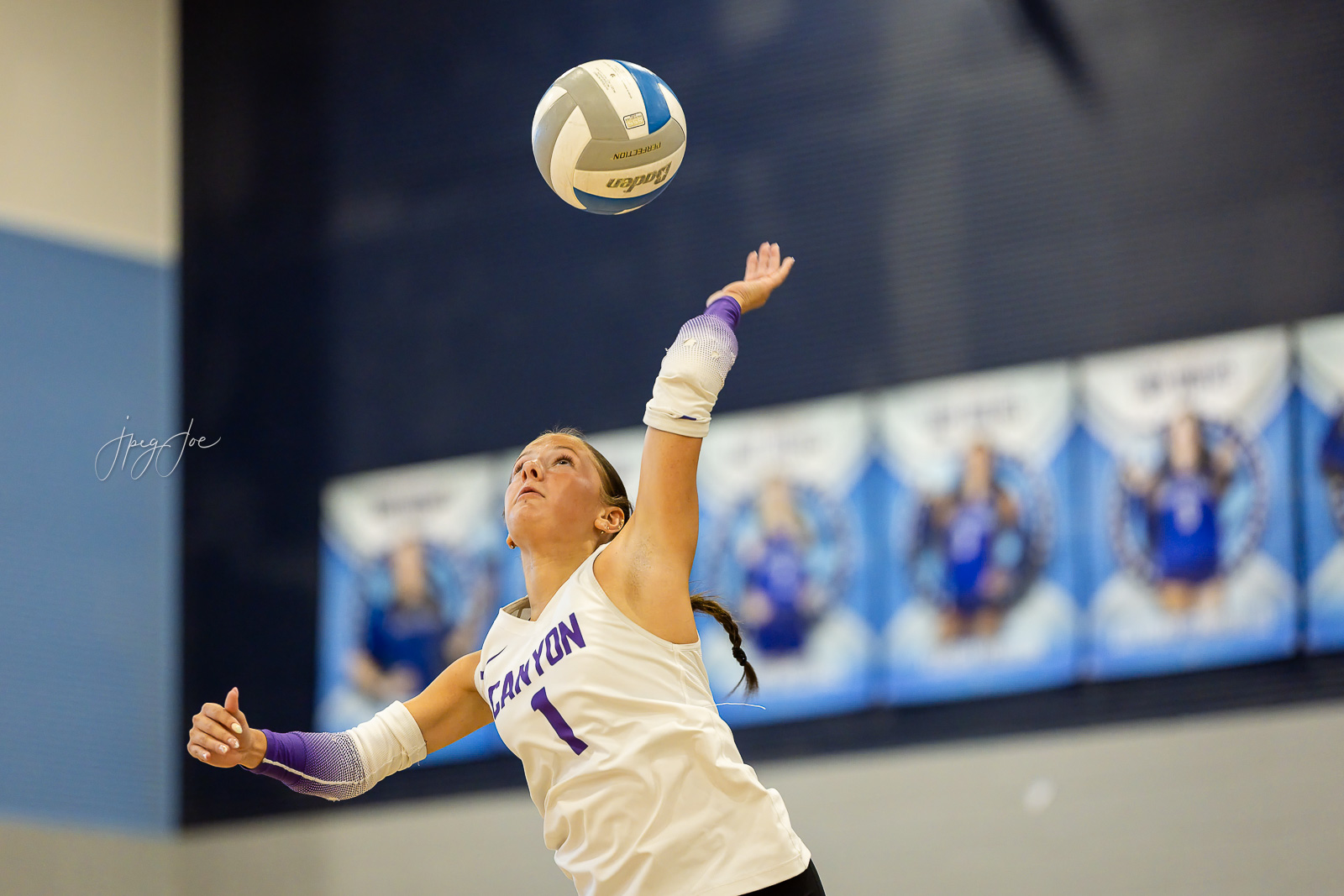 canyon-vs-west-plains-jpegJoe-volleyball-pps-14 | Press Pass Sports Female volleyball player in a white jersey (number 1) reaching up to spike the ball during a match in an indoor gym.