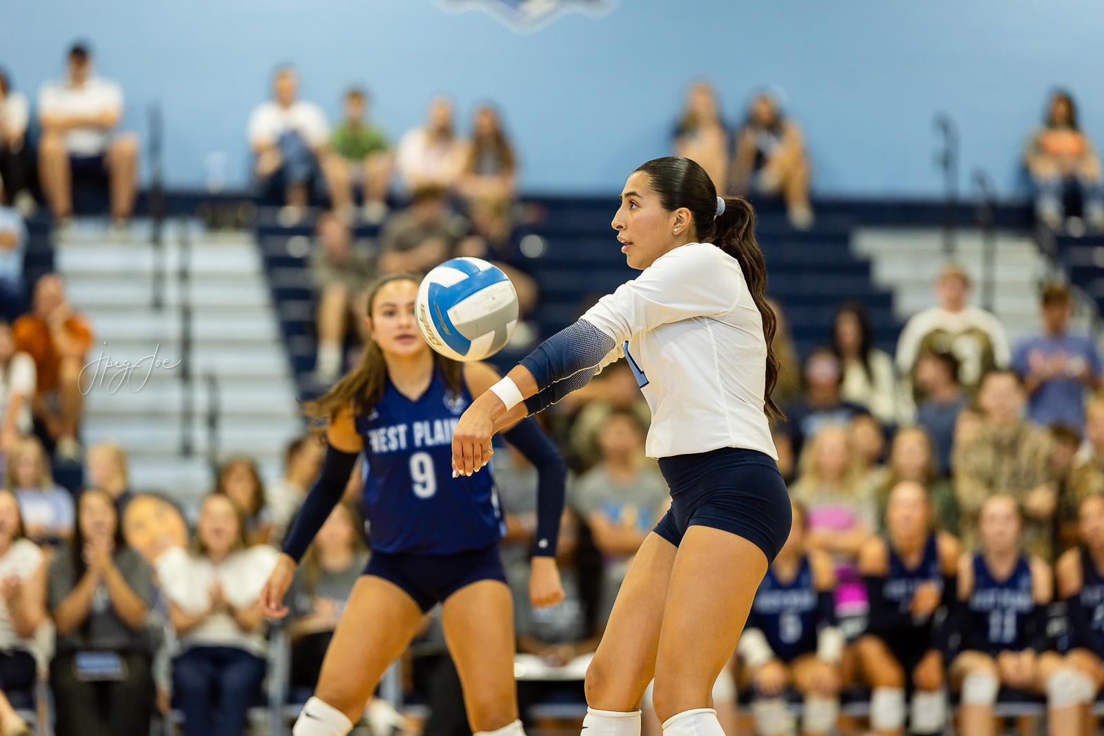 canyon-vs-west-plains-jpegJoe-volleyball-pps-20 | Press Pass Sports Volleyball player in white uniform bumps the ball during a match, with a crowded gymnasium in the background.