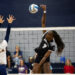 RHS-WPHS-VB-7 | Press Pass Sports Player in a black jersey jumps to spike the ball over the net as a defender in white reaches up to block the shot.