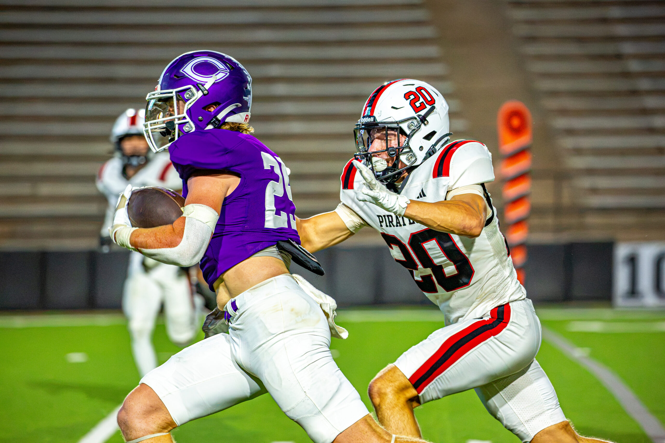 _v4a3260 | Press Pass Sports Two football players in purple and white uniforms collide on a bright turf during a game, one with the football tucked under his arm.