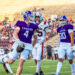 Canyon football player in purple jersey runs with the ball as teammates and opponents pursue on a sunny stadium field.