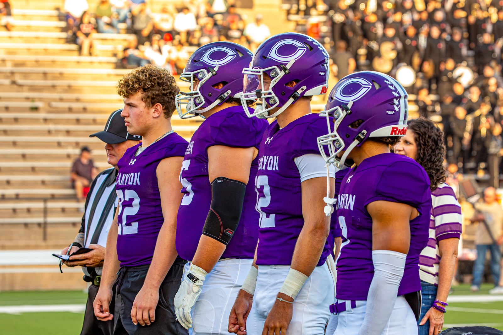 _V4A2697 | Press Pass Sports Football players in purple uniforms stand in a line on the field with a crowd in the bleachers behind them.